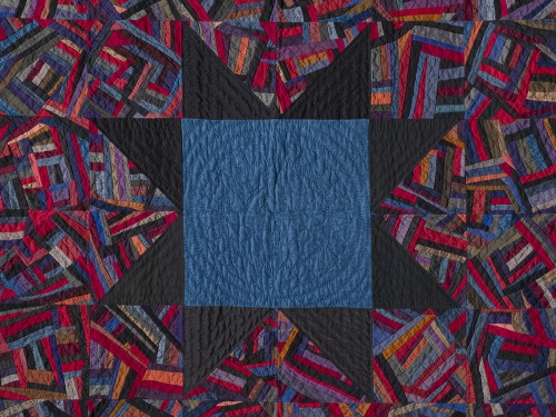 Multicolored quilt with repeating patterns and large blue square in center.