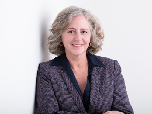 Woman in dark blazer smiles against white backdrop.